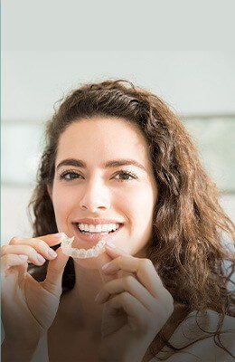 Smiling woman putting a clear aligner in her mouth