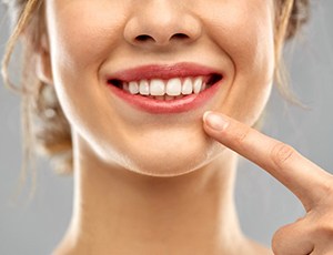 close up of woman pointing to her smile with straight white teeth 