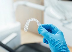 Dentist with blue glove holding clear aligner