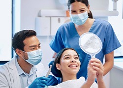 Patient smiling at reflection with dentist and dental assistant