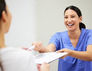 An oral hygienist giving a patient several dental insurance forms to sign