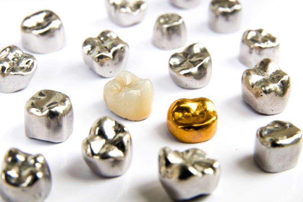 A tooth-colored and gold crown among many silver ones on a white surface